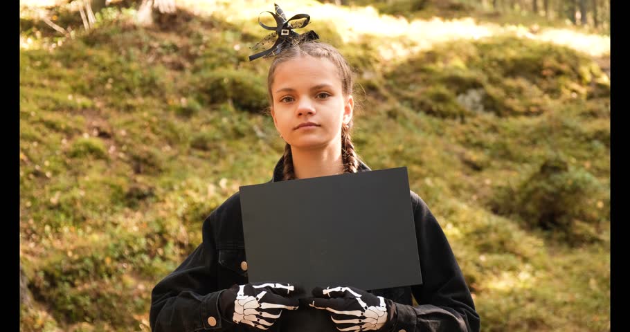 13 year old girl in gloves with bones print in halloween costume holding black blank sign for your text 4k