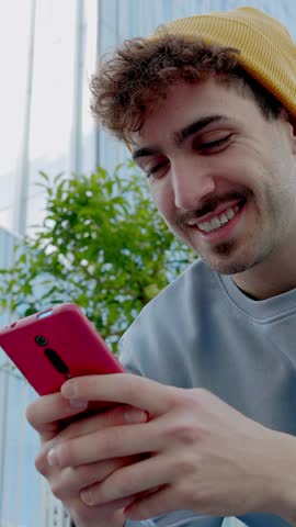 Vertical HD video. Low angle view of young college hipster student man using mobile phone outdoors. Technology lifestyle and social media concept.