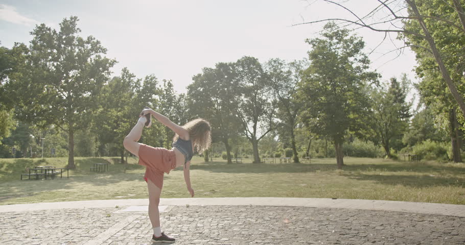 Young woman warms up for her workout with some stretches and leg raises in a sunny park.