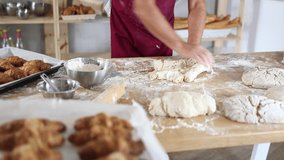 Close-up of professional male baker hands in dark red apron kneading dough on flour-dusted wooden table in artisan bakery, highlighting craftsmanship of traditional breadmaking. High quality 4k - Powered by Shutterstock - Get 15% off with code: PIKWIZARD15