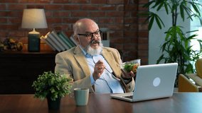 Indian Asian elderly businessman sporting a beard in a suit, attending a video call on his laptop in modern set up while enjoying a midday snack of salad and coffee, balancing work and health - Powered by Shutterstock - Get 15% off with code: PIKWIZARD15