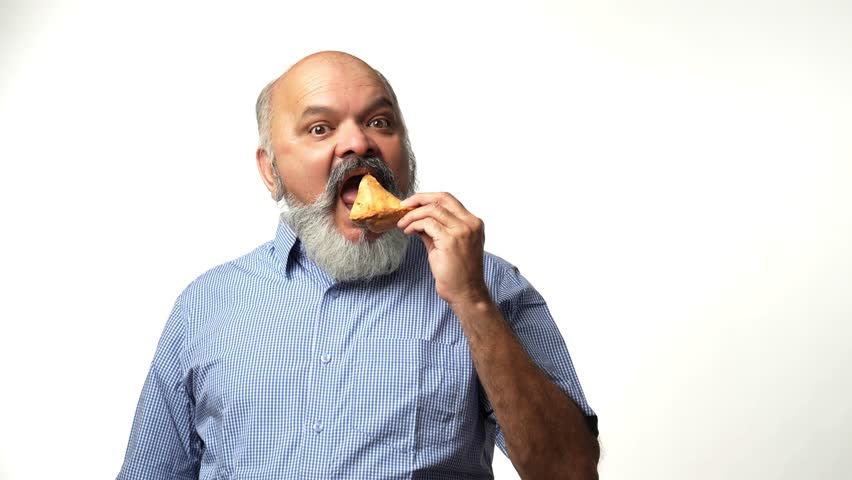 Indian Asian elderly gentleman with a beard enjoys a samosa secretely ,showing love for Indian snacks