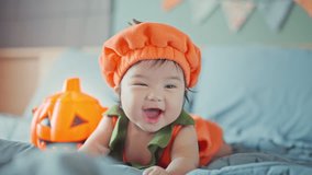 Happy cute asian newborn baby girl dressed in Halloween jack o lantern costume during tummy time on bed with Halloween decoration, having fun and celebrating Halloween at home - Powered by Shutterstock - Get 15% off with code: PIKWIZARD15