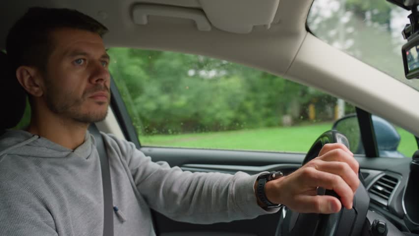 Man driving car on rainy day, maintaining focus on road. Male driver driving car looking around at road traffic and turning steering wheel. Safety ride