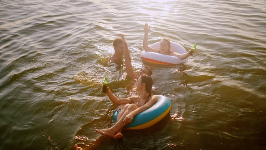 Group of friends having fun and enjoying a summer day swimming with rubber tube and drinking beer at the lake.