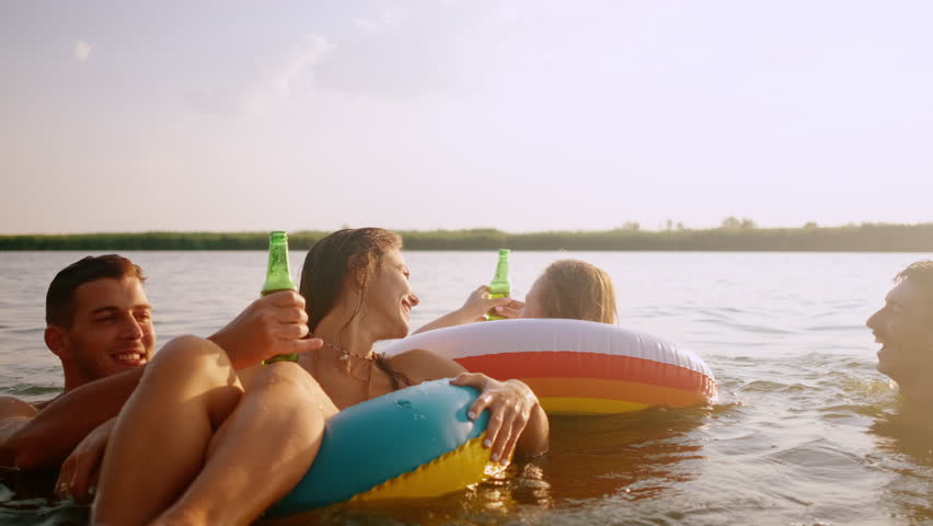 Group of friends having fun and enjoying a summer day swimming with rubber tube and drinking beer at the lake.
