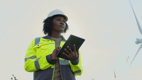 Focused African American woman holding tablet device while tapping on screen with one finger. Recording her observations from checking wind turbine power plant. Protective equipment. - Powered by Shutterstock - Get 15% off with code: PIKWIZARD15