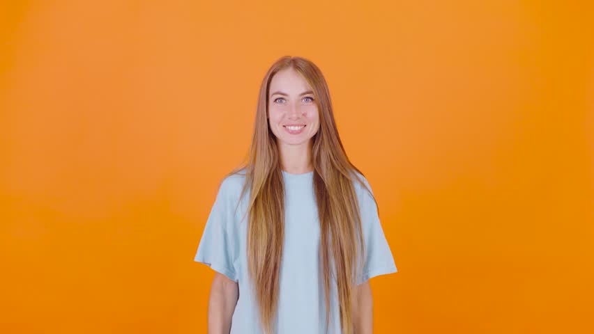 A young woman with long hair points downward, possibly towards an important message or advertisement. She s dressed casually and stands against an orange background