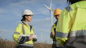 Experiences Caucasian male holding tablet device while standing next to working wind turbine with his colleagues. Giving tasks to optimize work flow. Planning new project together. Engineers. - Powered by Shutterstock - Get 15% off with code: PIKWIZARD15