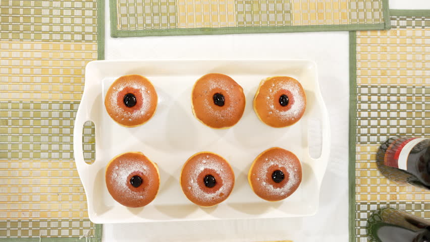 Hanukkah table decorated with golden sufganiyot, a braided challah, and blue and white cookies shaped like dreidels and Stars of David.