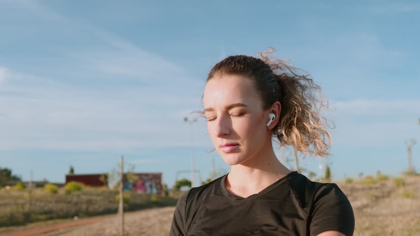 A close-up of a smiling sporty Caucasian girl checking the time while performing exercises in a park at sunset. Her cheerful demeanor highlights the joy of staying active in a beautiful summer setting