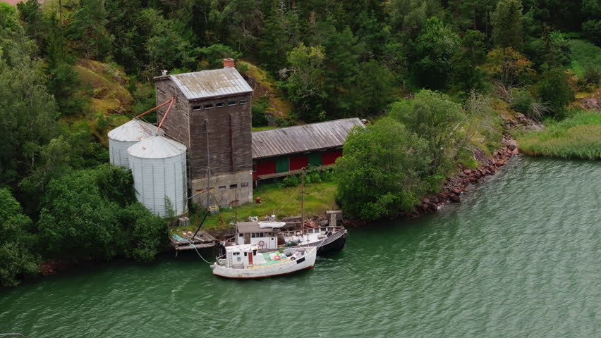 Two boats glide toward a weathered grain elevator along the Aland islands