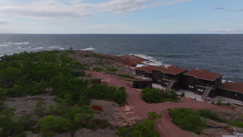 Aerial views highlight contemporary homes with dark wood and red roofs, nestled along a rugged coastline in Aland, Finland. The landscape beautifully merges nature and modern architecture