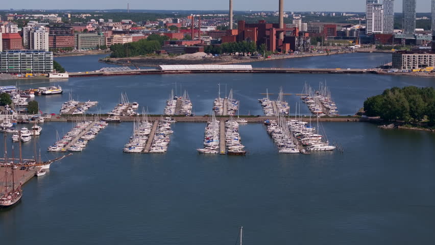 Aerial view of sailboats docked in Helsinki harbor on a sunny summer day. The camera pans slowly to reveal the cityscape of Finland