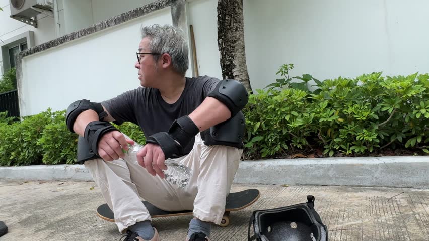 The senior Asian man is trying to ride a skateboard in the village during the daytime