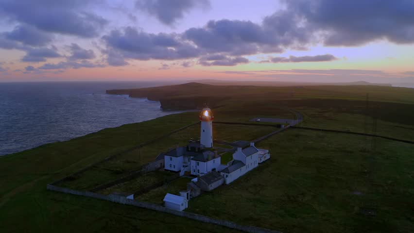 Stunning aerial orbit of Loop Head lighthouse, glowing in vibrant dawn colors over the dramatic peninsula. County Clare