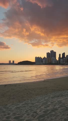 Sunset at Haeundae beach in Busan, South Korea. There are apartments and small hills shown.