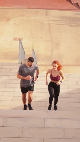 Vertical. Sporty couple running up stairs to improve their leg muscles. Athletic young friends doing cardio training on a stairway. Man and woman jogging doing a endurance workout outdoors with energy