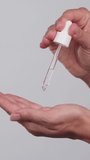 Close-up of female hands on isolated grey background holding dropper, anti-aging facial serum, booster dripping on palm. Skin care, moisturizing, vitamin c, anti-wrinkle, face lifting, anti-acne serum - Powered by Shutterstock - Get 15% off with code: PIKWIZARD15
