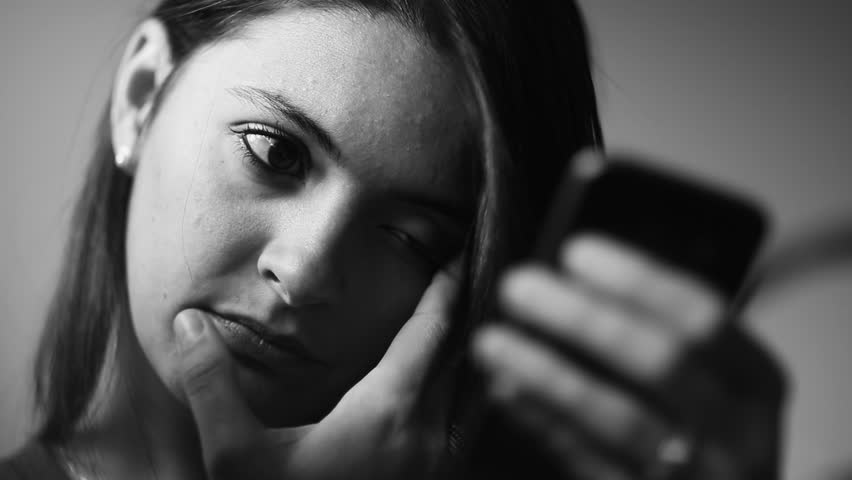 Woman holding smartphone with a distant expression, chin resting on her hand as she gazes at the screen. Reflecting a quiet and thoughtful interaction with technology