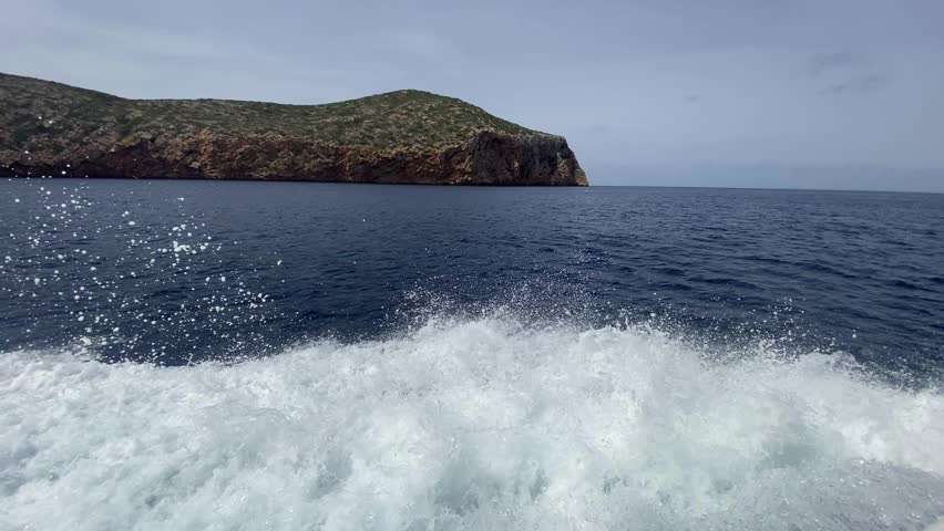 Large ship waves with white foam coming from a boat leaving at high speed from the wild cliffs of the National Park on the island of Cabrera. Cabrera Archipelago, Balearic Islands, Spain.