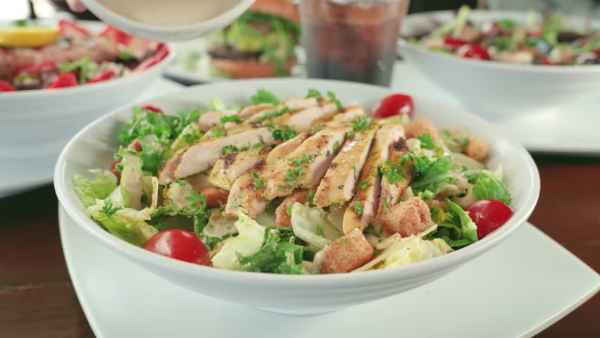 Bowl of Grilled Chicken Salad with a dressing pour over croutons and cherry tomatoes.