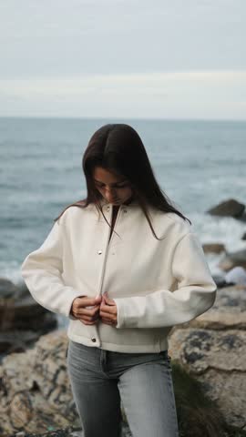 Beauty, fashion portrait of woman, model on the ocean shore in the rocks, soft comfortable clothes, campaign, posing, style, freedom, care, white jacket, twilight, portrait, vertical, face, glamor