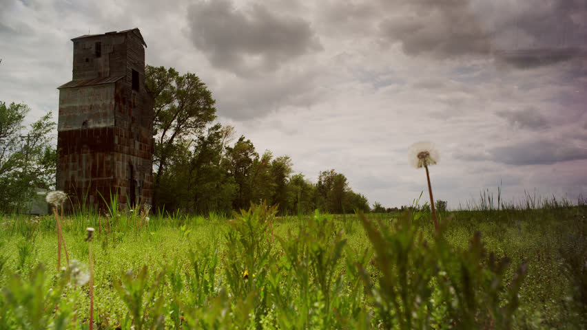 Old grain mill on a restored prairie bathed with sunshine, strong winds and the possibility of springtime storms.