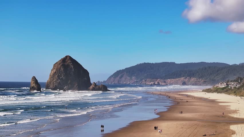 Tourists Strolling On Cannon Beach With Haystack Rock At The Shoreline In Clatsop County, Oregon. Slow Motion Shot