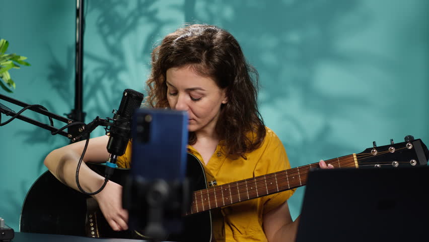 Talented woman playing music on guitar during livestream with audience online. Musician using musical instrument, having fun doing concert for fans producing entertaining songs, camera A