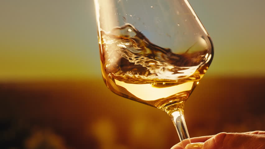 Orange or white wine bottle and glass against a sunset in a peaceful vineyard, pouring of ecological natural wine. 