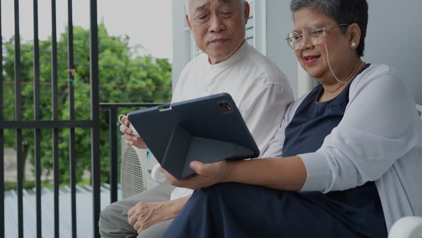 Two elderly individuals enjoy a light-hearted conversation and laughter on a balcony, sharing a peaceful and joyful moment in a relaxed outdoor setting, highlighting friendship and companionship.