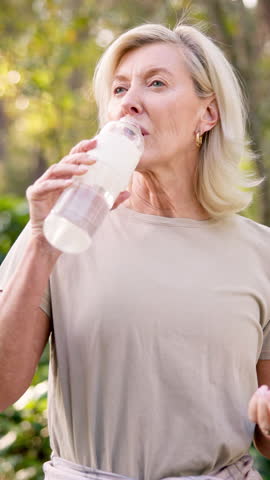 Outdoor, drinking water and mature woman with fitness, nature and wellness with balance. Pensioner, runner and athlete in park, liquid and nutrition with challenge, exhausted and workout with health