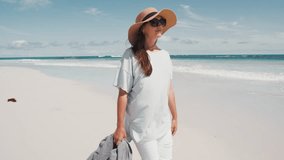 A woman walks barefoot on a beautiful sandy beach, holding a jacket and enjoying the warm sun and calm waves under a clear blue sky. - Powered by Shutterstock - Get 15% off with code: PIKWIZARD15
