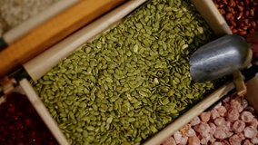 Hand scooping pumpkin seeds from a paper bin at a bulk food store. Close-up of seeds in a wooden container surrounded by other dried goods - Powered by Shutterstock - Get 15% off with code: PIKWIZARD15