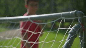 A blurred view of a goalkeeper in red attempts to save a ball shot into the net in a grassy field - Powered by Shutterstock - Get 15% off with code: PIKWIZARD15