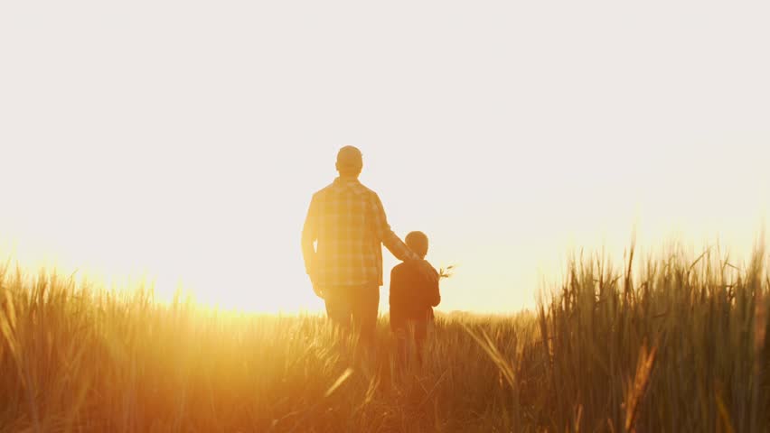 Farmer and his son in front of a sunset agricultural landscape. Man and a boy in a countryside field. Fatherhood, country life, farming and country lifestyle concept.