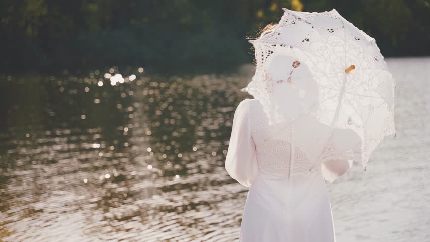 happy woman holds white lace umbrella in hands, vintage dress old style. Noble lady queen back rear view, stands by river bank girl looking at shiny water green trees fairy nature sun light day art 4k