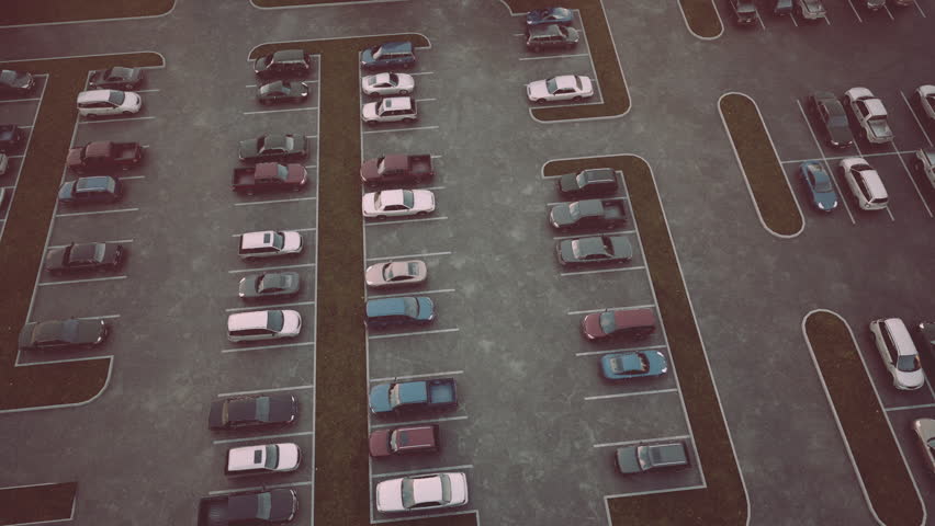 An aerial perspective shows a nearly full parking lot during sunset. Vehicles occupy numerous spots, creating a busy atmosphere as shoppers return from their day.