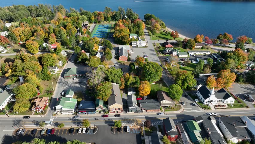 Aerial view of Schroon Lake, New York, showcasing the calm lake, fall foliage, and small town structures nestled along the shoreline under a clear sky.