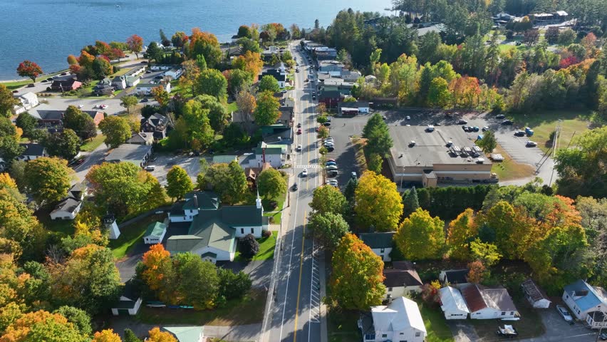 Aerial view of Schroon Lake, New York, showcasing the calm lake, fall foliage, and small town structures nestled along the shoreline under a clear sky.