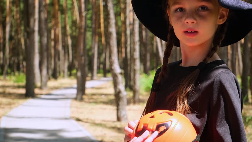 Child girl in carnival costumes witches holding a bucket for candy. trick or treating for halloween takes candy. Childhood, tradition and fun concept . Slow motion