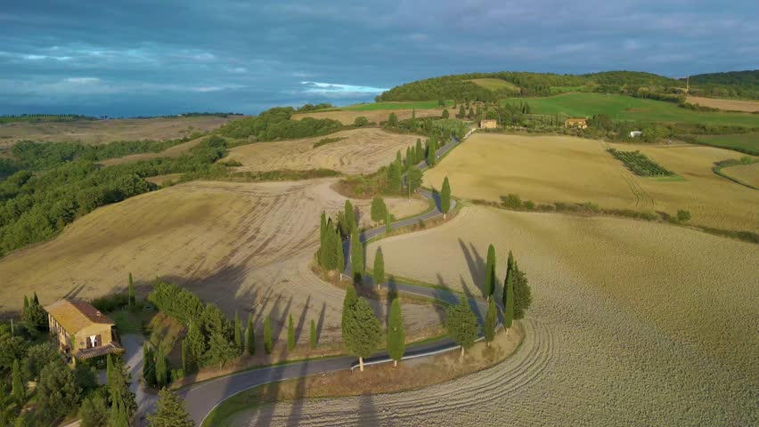 Experience Tuscany's beauty through stunning drone footage of rolling hills, lush greenery, and winding roads lined with elegant cypress trees, all painted in golden sunset light. Toscana Italy