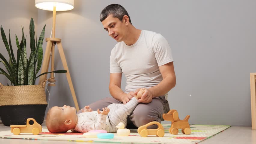 Tired Caucasian dad yawning while sitting with his newborn girl or boy on floor in living room at home father feeling fatigue while taking care of his infant child
