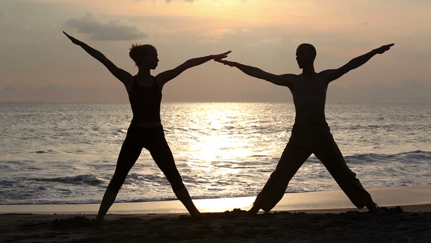 Couple doing exercise yoga on beach while sunset
