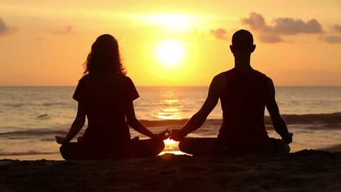 Couple sitting yoga on beach while sunset