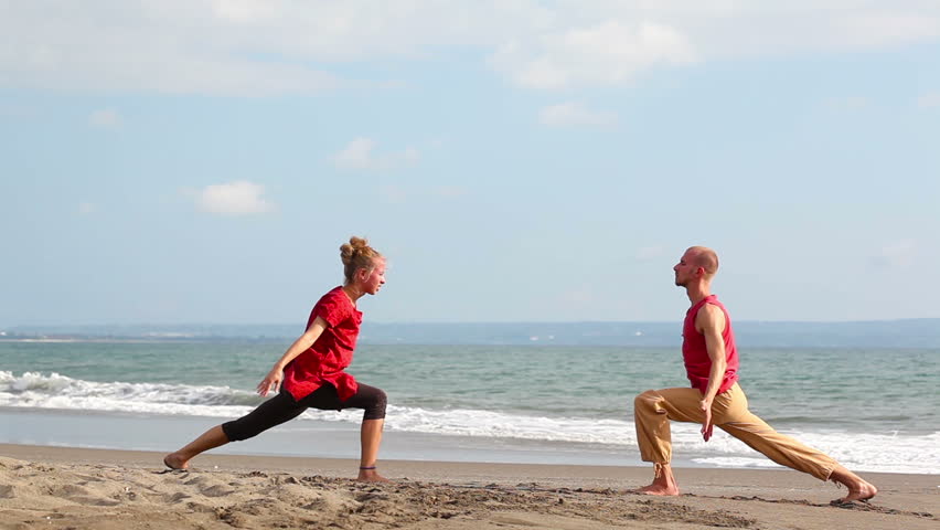 Peaceful pair practicing yoga together on beach
