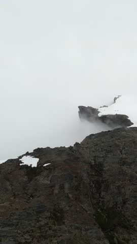 A slow pan across snow capped mountain peaks with fog and mist rolling through the valley below on a cold winter day. British Columbia, Canada.