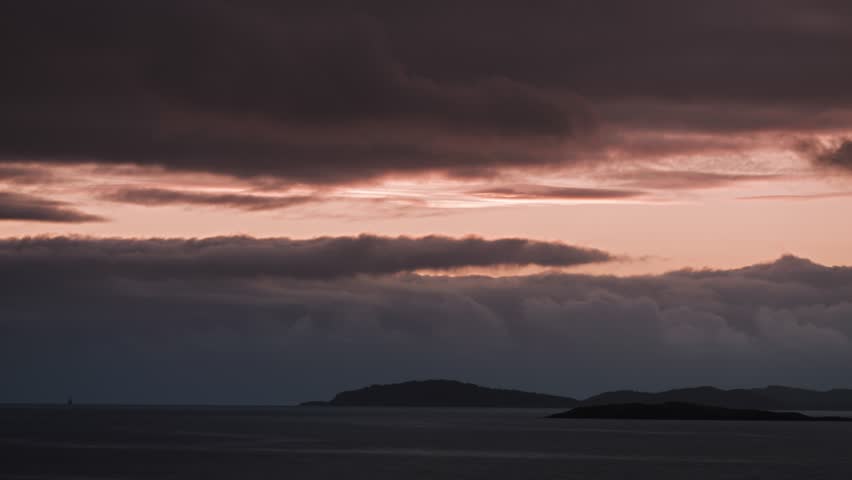 The soft glow of a setting sun casts a warm light over the horizon, with islands silhouetted in the distance.