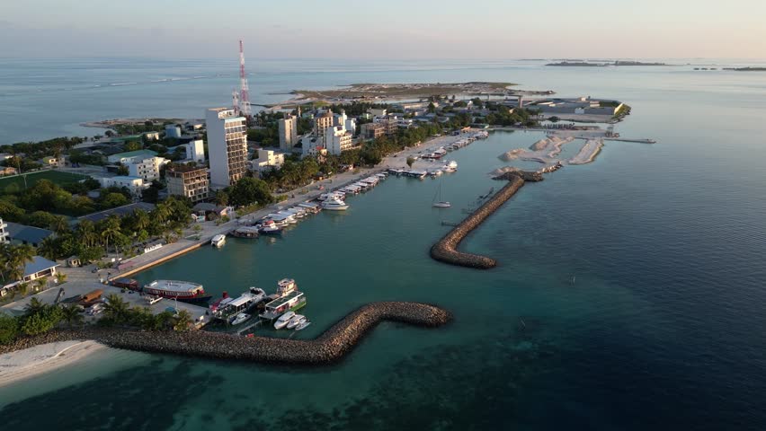 Aerial view of coastal town with a harbor, boats docked along the shore, and a protective breakwater. Maafushi Maldives.